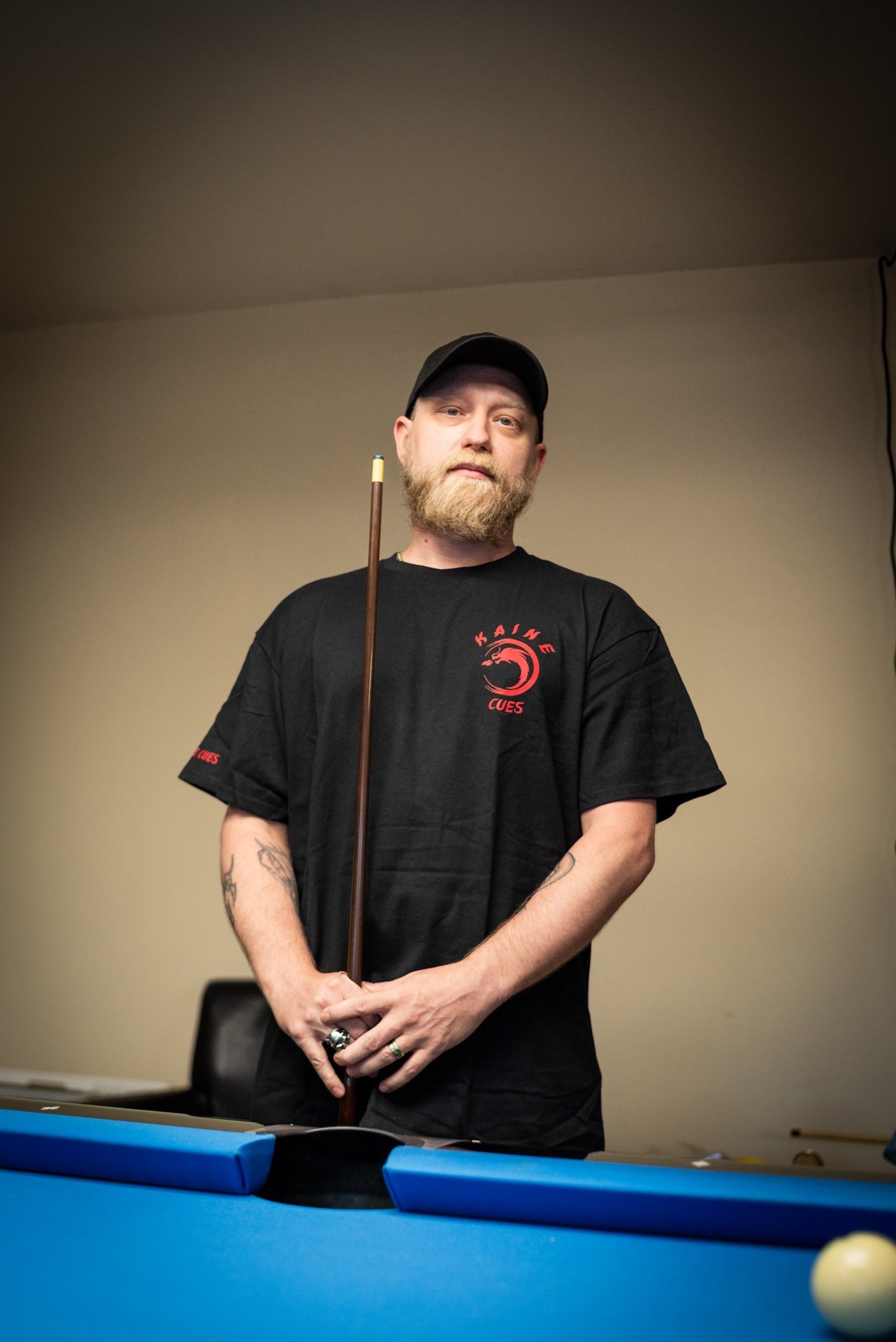 black kaine cues logo t-shirt worn by a team member against a neutral background.